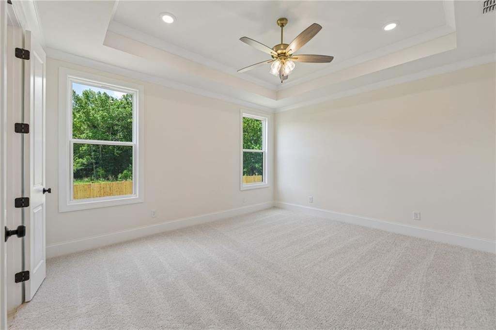 Spacious room featuring light-toned carpeting, a tray ceiling with a brass-finish ceiling fan, and recessed lighting