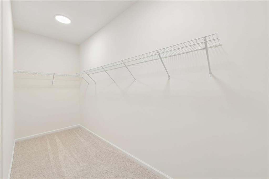 Spacious walk-in closet featuring light-colored carpeting, white walls, built-in wire shelving, and recessed ceiling lighting