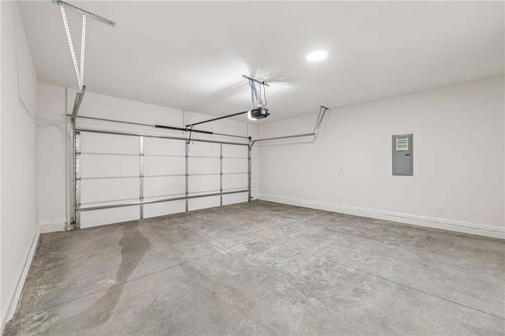 Spacious garage featuring a concrete floor, white walls, overhead lighting, and an automatic garage door opener