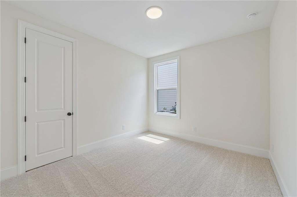 Neutral-toned room featuring a single window with blinds, light-colored carpet, a flush-mount ceiling light, and a white two-panel door with a black doorknob