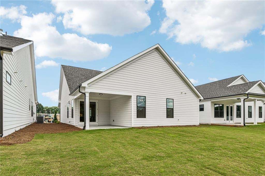 Rear exterior featuring a covered patio with a concrete slab, white siding, black-framed windows, and a manicured lawn
