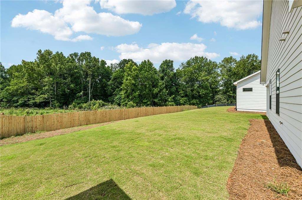 Spacious green lawn with a newly installed wooden privacy fence, backed by mature trees