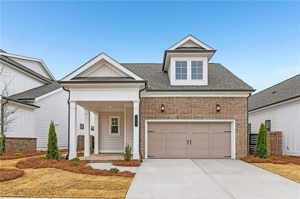 View of front of home featuring brick siding, roof with shingles, covered porch, and driveway