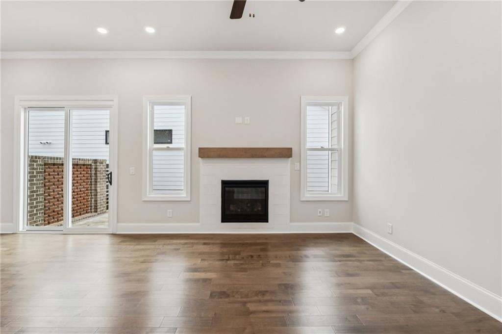 Unfurnished living room with a glass covered fireplace, a ceiling fan, dark wood-type flooring, ornamental molding, and recessed lighting