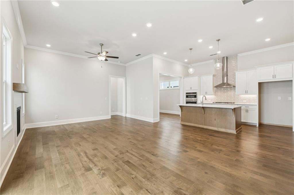 Unfurnished living room featuring a large fireplace, recessed lighting, ceiling fan, dark wood-style flooring, and crown molding