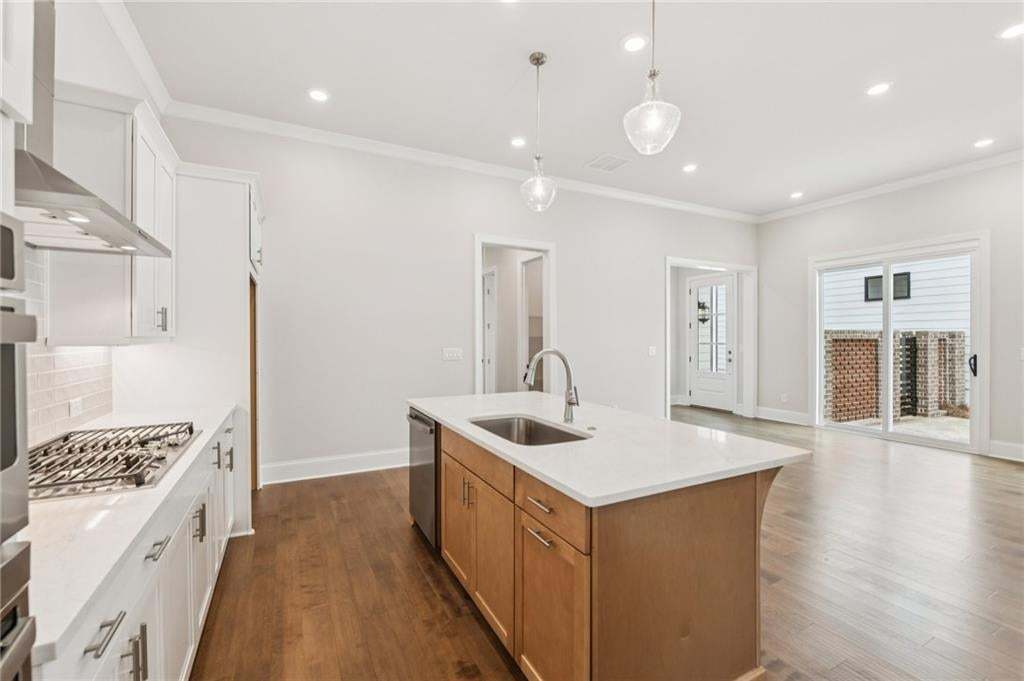 Dual tone kitchen featuring light stone countertops, two tone color scheme, dark wood-style flooring, ornamental molding, and a kitchen island with sink