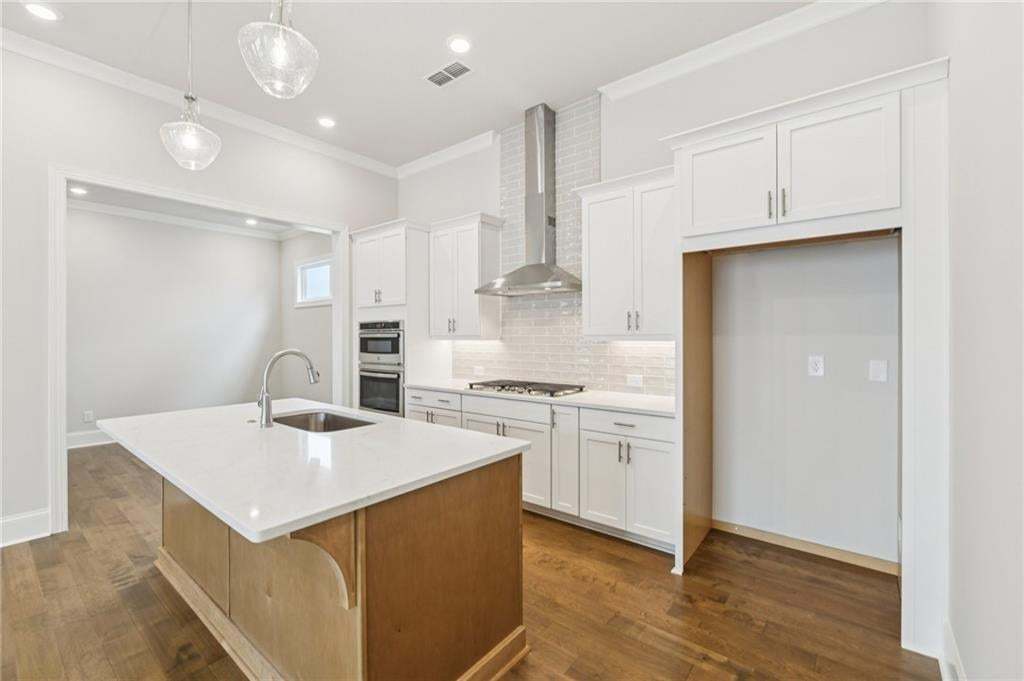 Kitchen with a center island with sink, crown molding, dark wood finished floors, tasteful backsplash, and stainless steel appliances