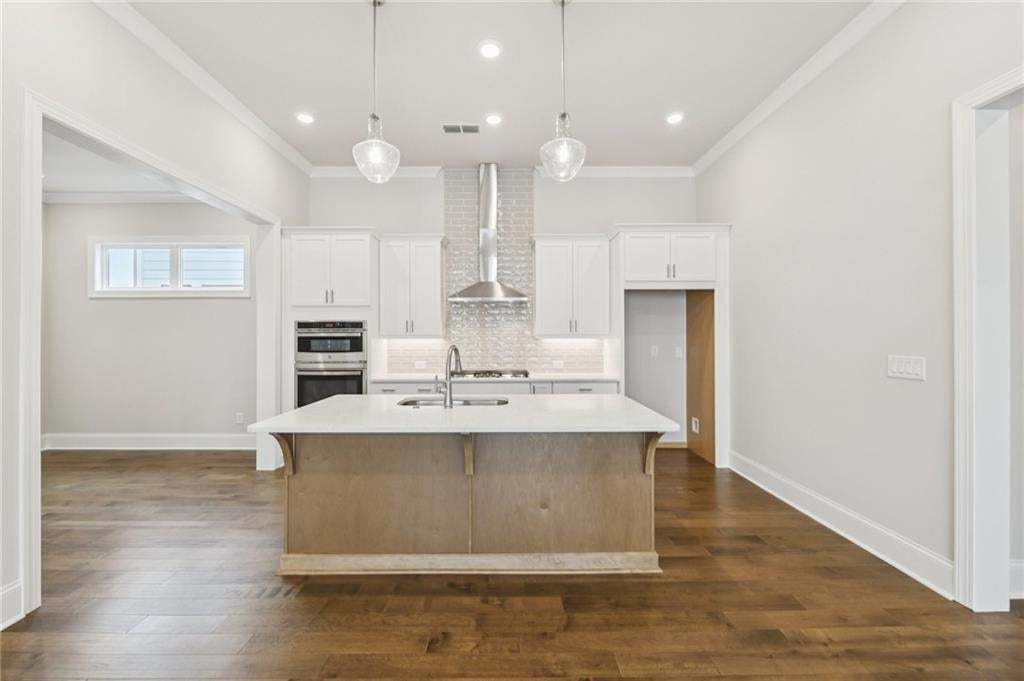 Kitchen featuring a kitchen island with sink, decorative backsplash, dark wood-style floors, a breakfast bar, and hanging light fixtures