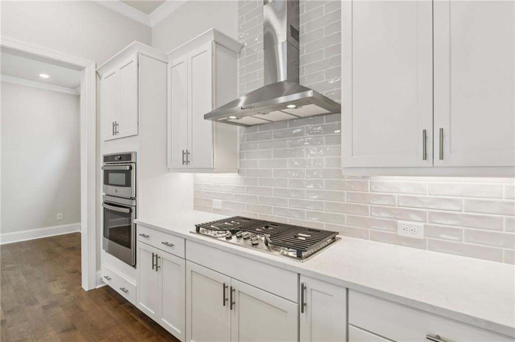 Kitchen featuring crown molding, dark wood finished floors, light stone counters, white cabinets, and stainless steel appliances