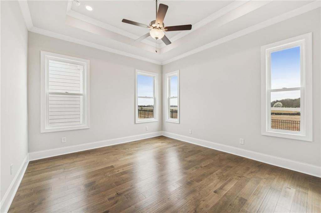 Empty room with a ceiling fan, dark wood-style floors, and crown molding