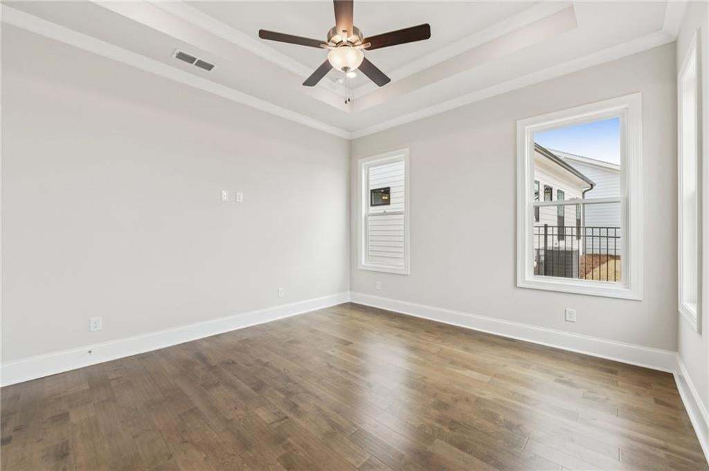 Empty room with dark wood finished floors, ceiling fan, a tray ceiling, and crown molding
