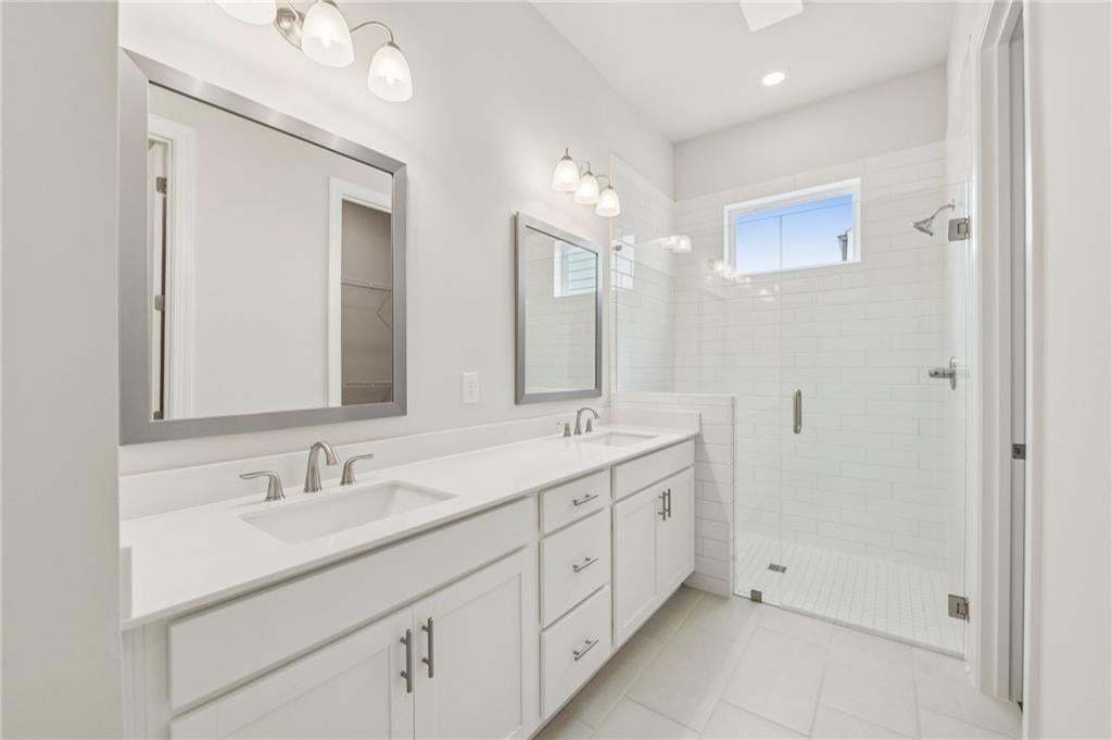 Full bath featuring double vanity, a shower stall, light tile patterned floors, a walk in closet, and recessed lighting