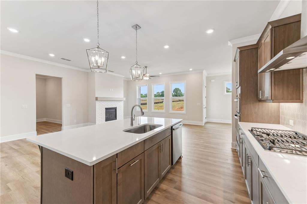 Open-concept kitchen featuring a large island with an undermount sink, quartz countertops, wood-finish flooring, recessed lighting, and a gas range
