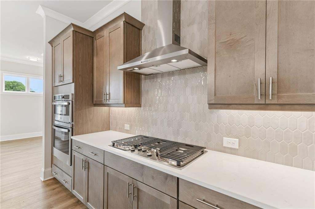 Modern kitchen featuring light wood-finish cabinetry, stainless steel appliances, a gas cooktop, white countertops, and a full-height geometric tile backsplash