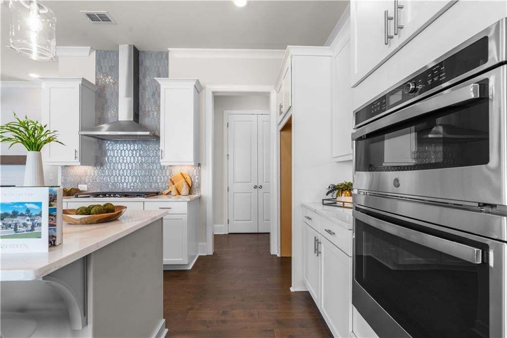 Modern kitchen featuring stainless steel double ovens, white cabinetry, a light-toned countertop, a tile backsplash, and dark wood-finish flooring