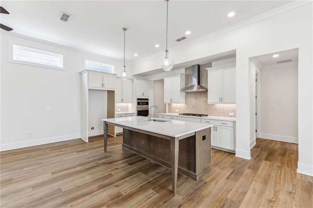 Kitchen featuring an island with stone countertop, stainless steel appliances, wood-finish flooring, recessed lighting, and upper transom windows