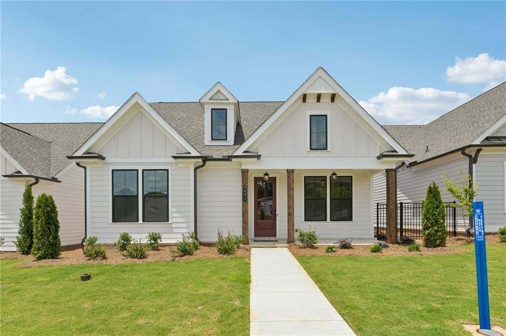 White siding home featuring a dark red entry door, decorative gables, black-trimmed windows, and natural wood-finish porch columns