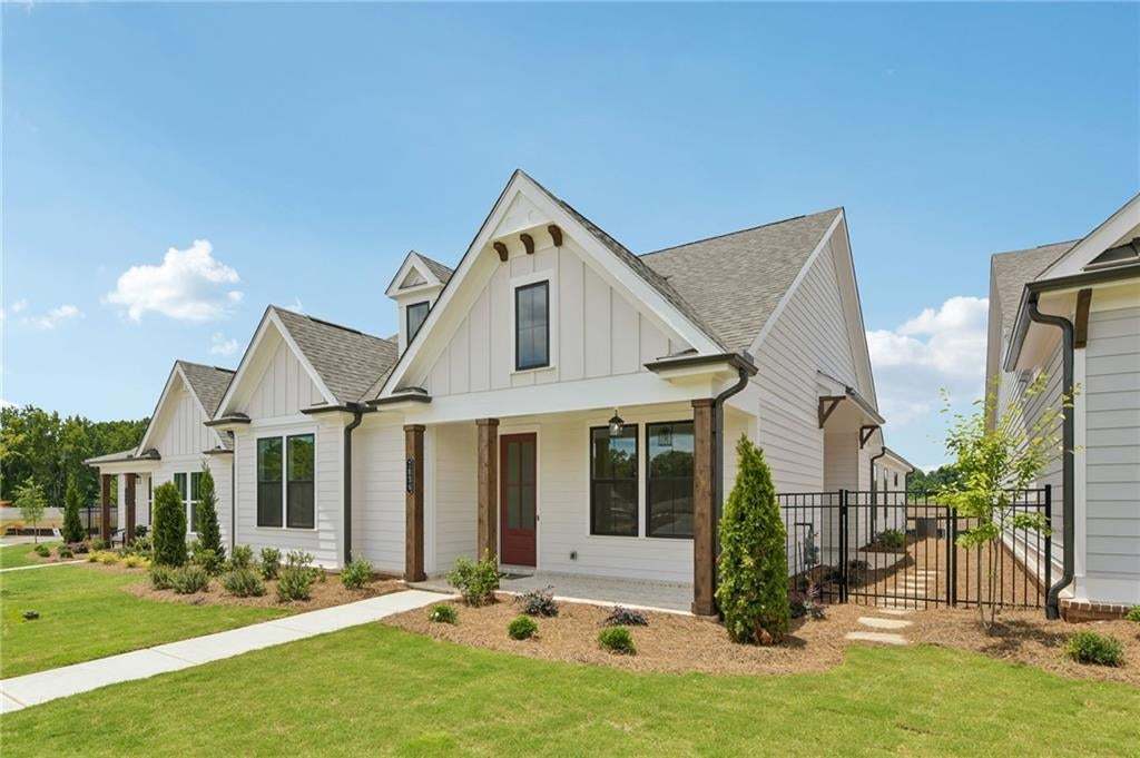 Modern farmhouse exterior featuring white board and batten siding, dark framed windows, a red entry door, natural wood columns, and a landscaped front yard with a concrete walkway