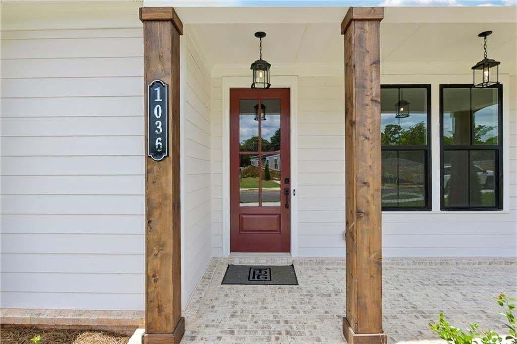 Inviting front porch featuring a rich red entry door with glass panels, light brick flooring, and robust wood-finish columns