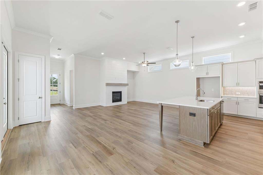 Open-concept living space featuring wood-finish flooring, a contemporary kitchen island with a sink, a built-in electric fireplace with a wood mantle, recessed lighting, and transom windows