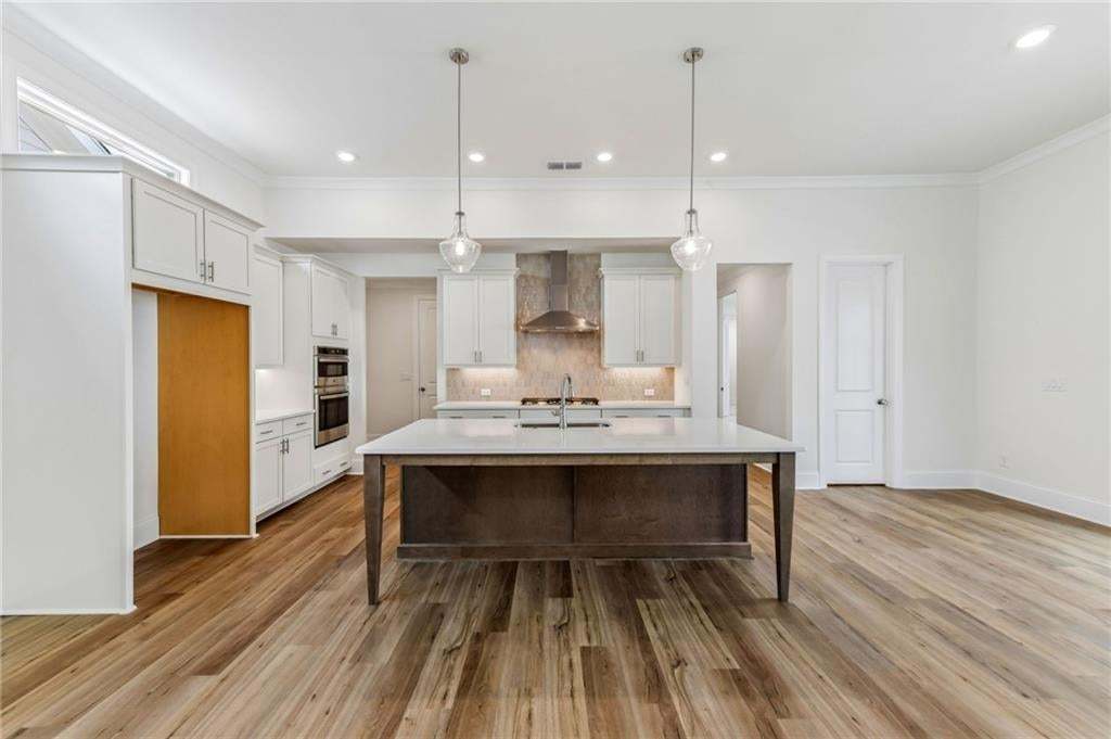 Spacious kitchen area featuring an expansive island with a light-toned countertop, white cabinetry with silver hardware, wood-finish flooring, and two modern pendant lights