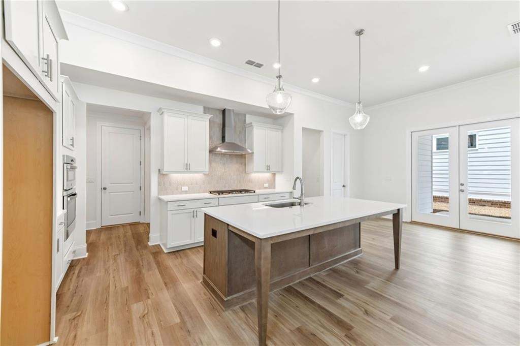 Kitchen featuring a large central island with a sink, wood-finish flooring, white cabinetry with modern hardware, stainless steel appliances, and double doors to the exterior