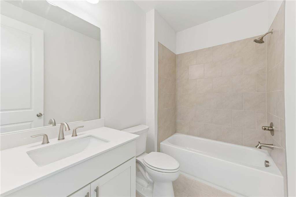 Bathroom featuring a white vanity with an integrated sink, brushed nickel fixtures, a full-width mirror, and a tub with tiled surround