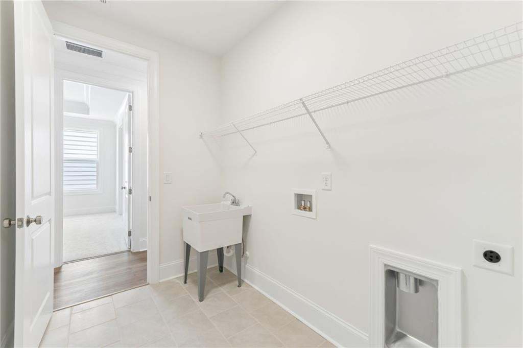 Utility room with a white utility sink, light-toned tile flooring, and a wire shelving system