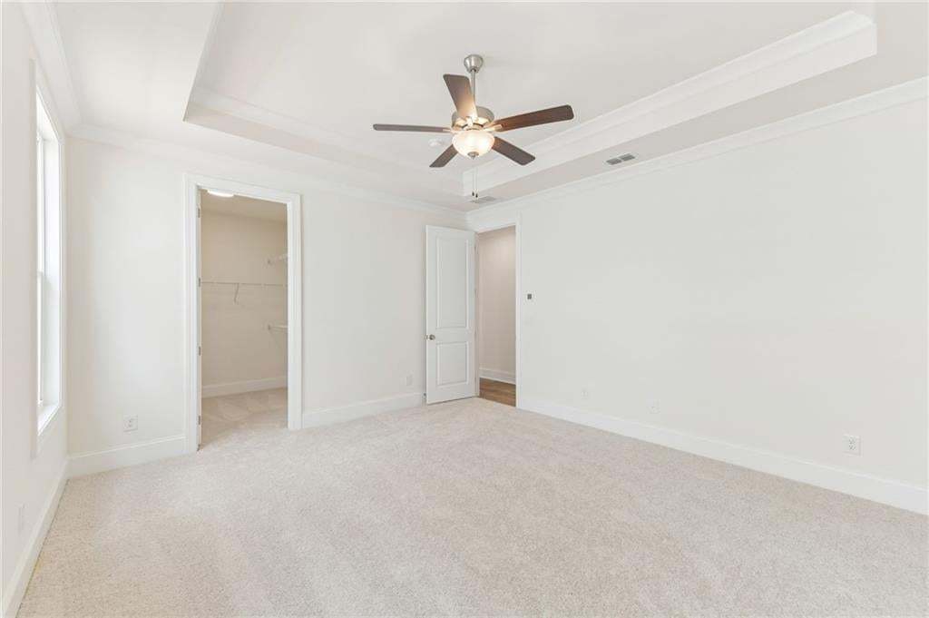 Spacious room featuring tray ceilings with crown molding, a ceiling fan with integrated lighting, and neutral carpet flooring