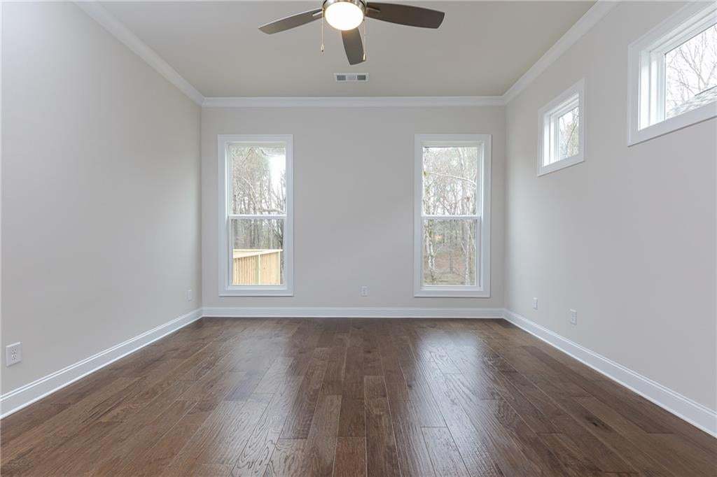 Spacious room featuring wood-finish flooring, multiple windows, a ceiling fan with integrated lighting, white trim, and a neutral wall color