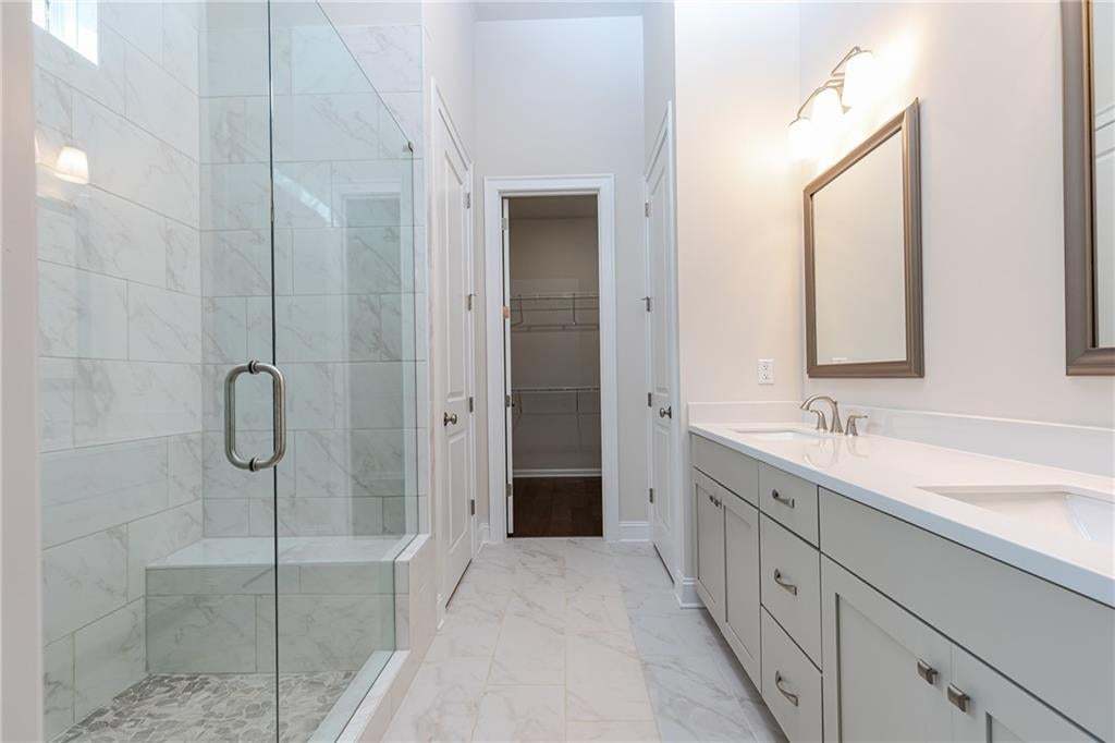 Tiled bathroom featuring a glass-enclosed shower with a built-in bench, dual vanity with undermount sinks, and a separate closet with wire shelving
