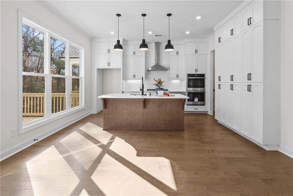 Bright kitchen featuring light wood-finish flooring, white cabinetry, a large central island with a contrasting base, and stainless steel appliances