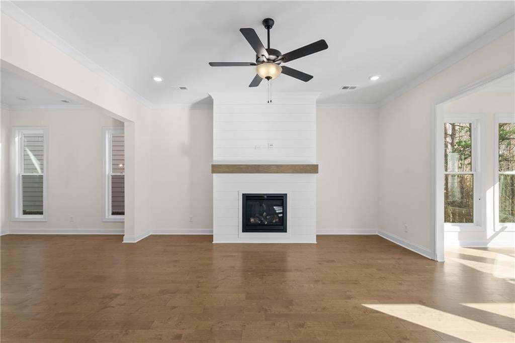 Open concept interior featuring wood-finish flooring, a contemporary kitchen with white cabinetry and a central island, recessed lighting, and a staircase with dark wood treads and an iron baluster