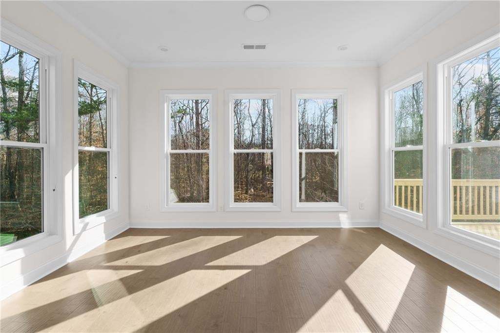 Spacious kitchen featuring an expansive center island with seating, white shaker cabinetry, wood-finish flooring, stainless steel double ovens, and a large window overlooking a deck