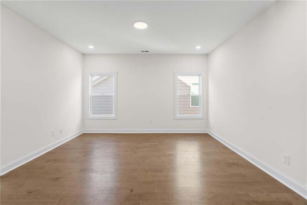Spacious room featuring wood-finish flooring, recessed lighting, and bright white walls