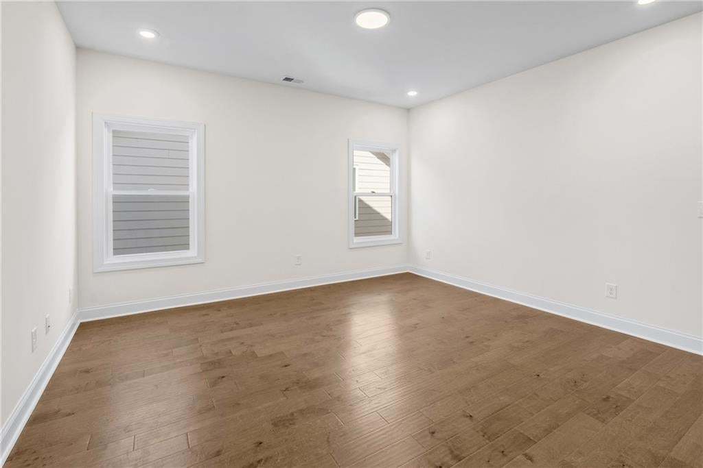 Spacious room with wood-finish flooring, white baseboards, and neutral wall paint