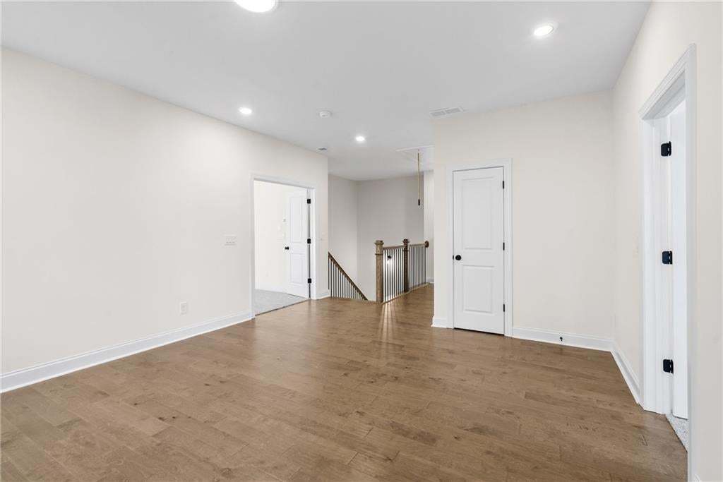 Expansive upper-level landing featuring wood-finish flooring, recessed lighting, white walls, white trim, and multiple white panel doors with black hardware