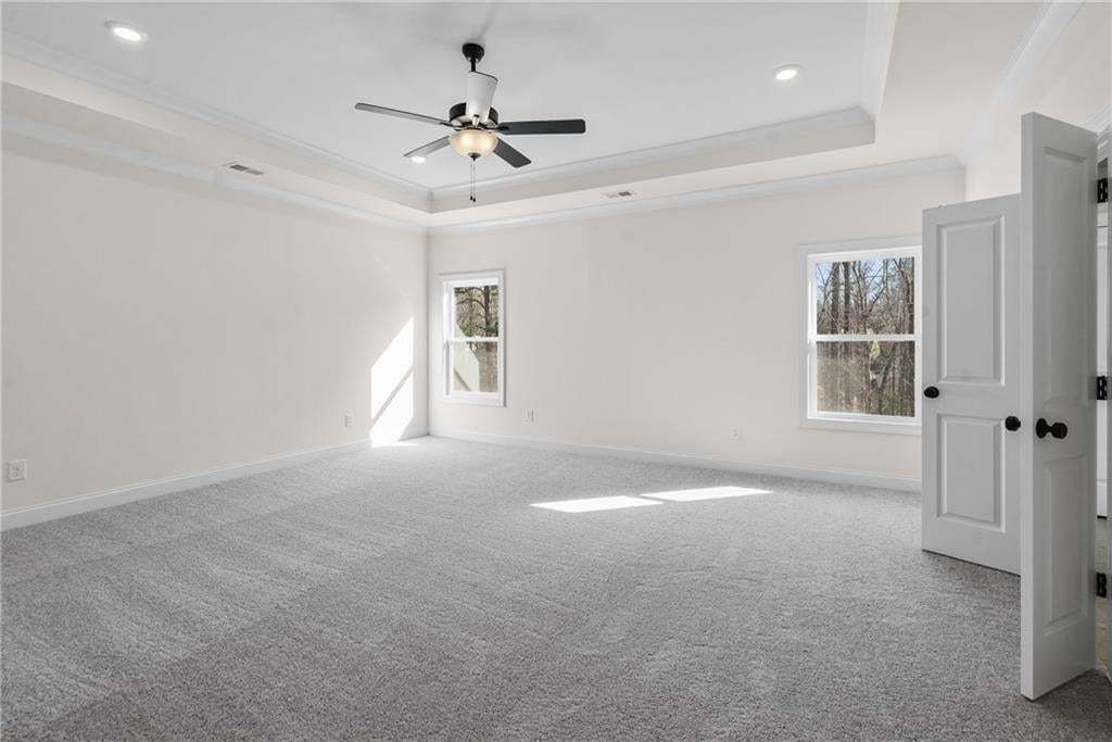 Spacious room featuring tray ceilings, recessed lighting, and a ceiling fan
