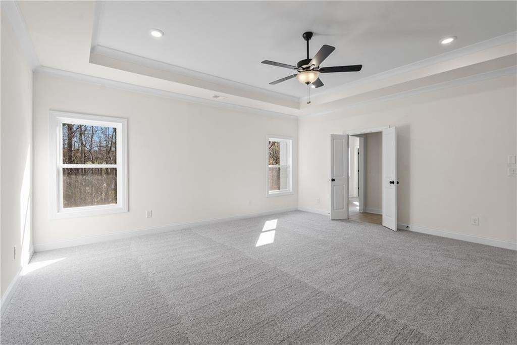 Spacious room featuring tray ceilings with crown molding, recessed lighting, and a ceiling fan