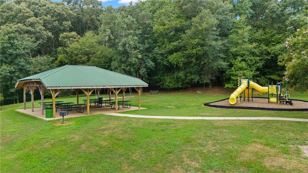 Expansive outdoor area featuring a covered picnic pavilion with a green metal roof, a dedicated playground area with a yellow slide, and verdant surroundings
