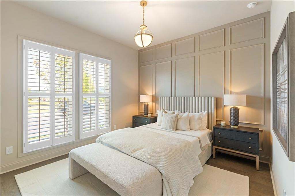 Paneled accent wall with integrated wall sconces, dual window openings with white plantation shutters, wood-finish flooring, and a ceiling-mounted light fixture