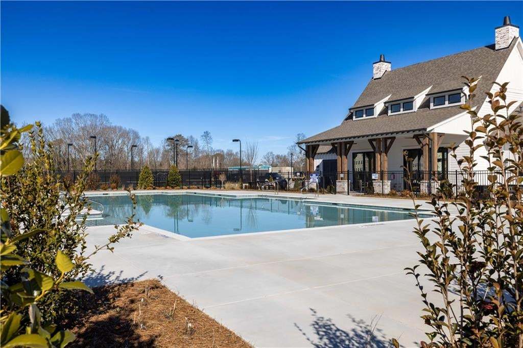 Expansive outdoor pool with a concrete surround, adjacent to a clubhouse featuring a gabled roof and dormer windows