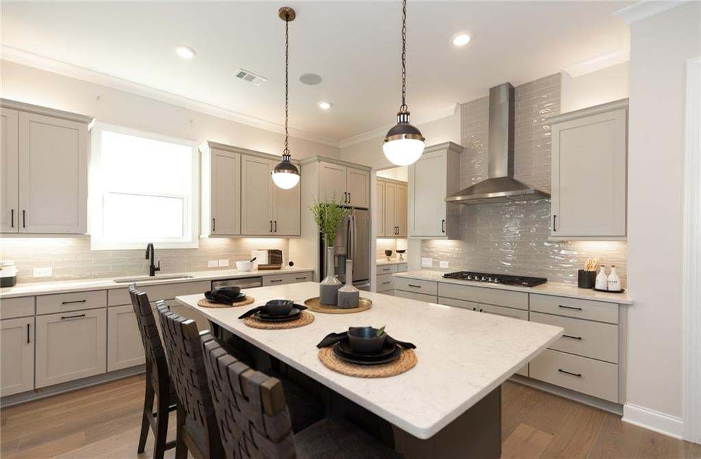 Kitchen featuring light-toned cabinetry, a spacious island with a light-toned countertop, wood-finish flooring, a stainless steel range hood, and pendant lighting