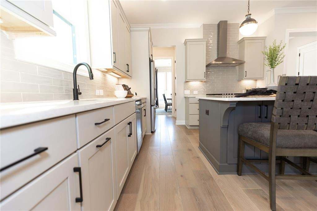 Kitchen featuring light wood-finish flooring, white cabinetry with matte black hardware, a subway tile backsplash, and a central island with an integrated cooktop
