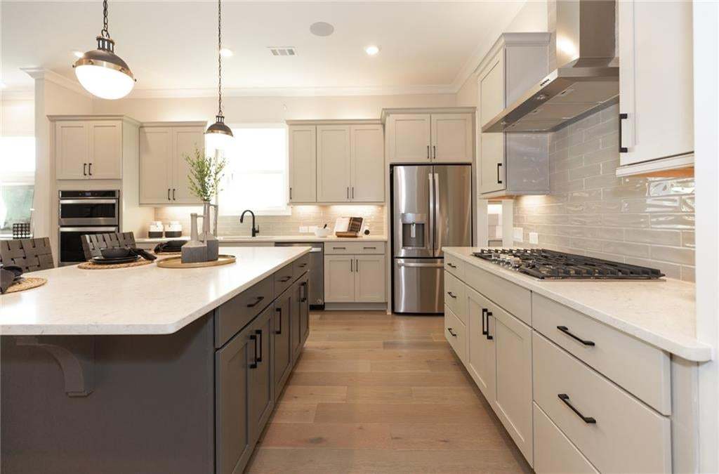 Contemporary kitchen featuring a large central island, light-toned cabinetry, stainless steel appliances, a gas range, and wood-finish flooring