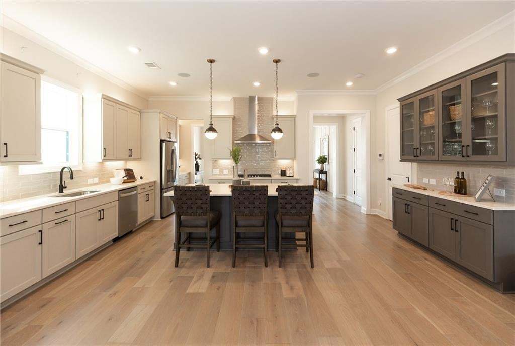 Gourmet kitchen with an expansive island, light wood-finish flooring, light-toned cabinetry, stainless steel appliances, and a built-in wet bar with glass-front display cabinets