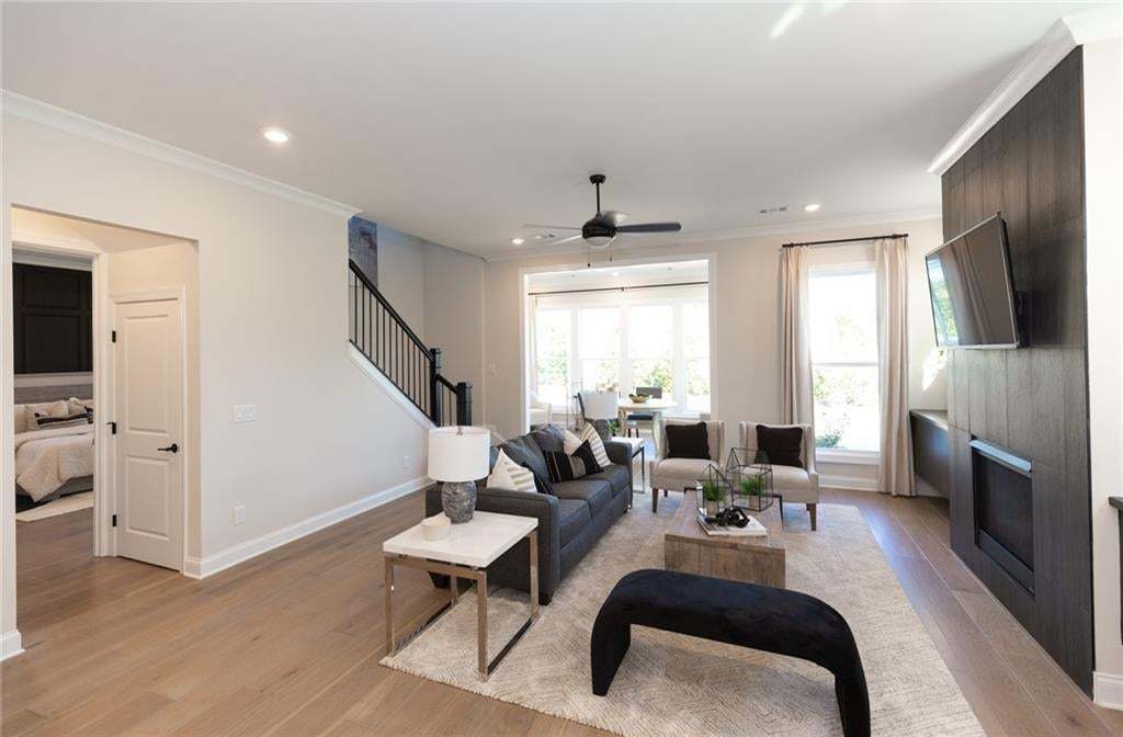 Spacious living area featuring light wood-finish flooring, a contemporary fireplace with dark wood paneling, and an open concept layout with ample natural light from large windows