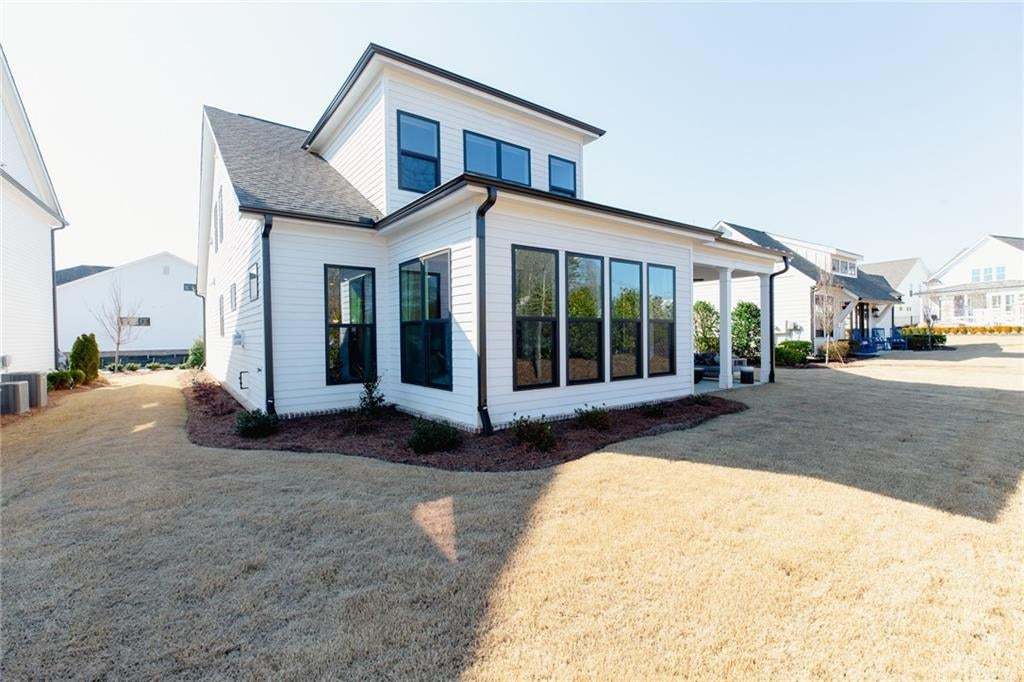 Contemporary white siding exterior, large black-framed windows, integrated covered patio, dark asphalt shingle roof, and rain gutters