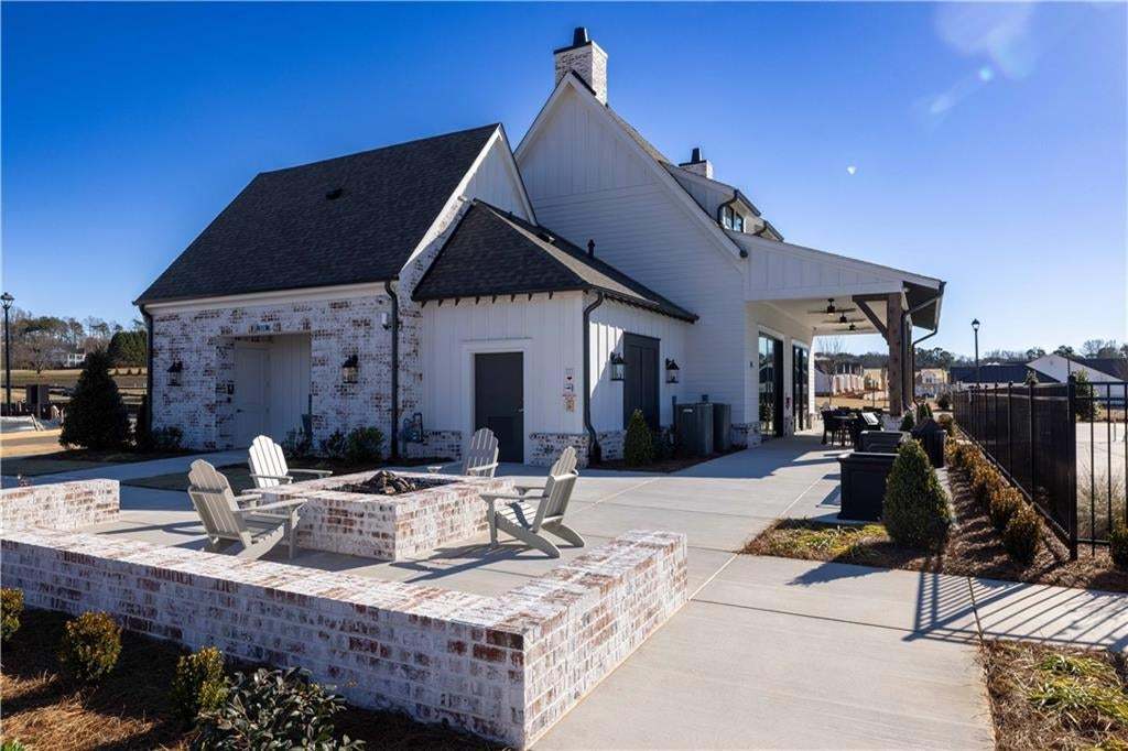 White board-and-batten siding with brick accents, covered outdoor living area, built-in fire pit with brick surround, and concrete hardscaping