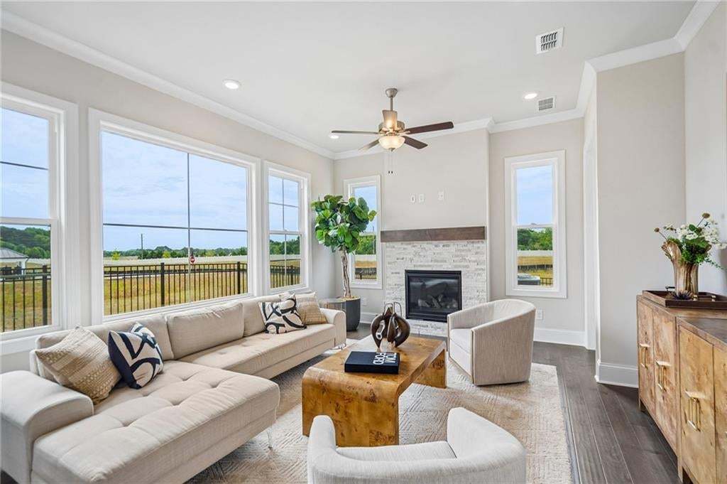 Living area featuring a stone-clad fireplace with a wood mantel, dark wood-finish flooring, white crown molding, and recessed lighting